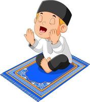 the boy is praying and sitting on the blue prayer rug vector