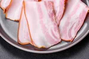 Delicious fresh raw bacon cut with slices on a grey plate against a dark concrete background photo