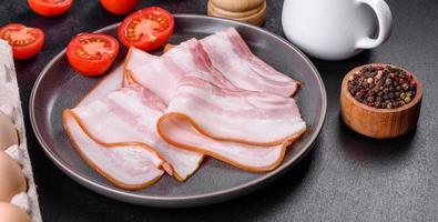 delicioso tocino crudo fresco cortado con rodajas en un plato gris sobre un fondo de hormigón oscuro foto