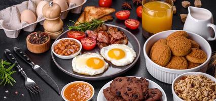 A delicious nutritious healthy breakfast with fried eggs, bacon, beans, a glass of juice, oat cookies, milk and jam photo