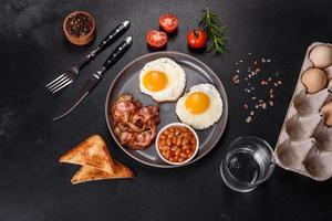 A delicious nutritious healthy breakfast with fried eggs, bacon, beans, a glass of juice, oat cookies, milk and jam photo