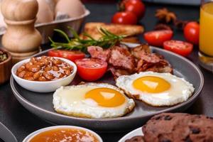 A delicious nutritious healthy breakfast with fried eggs, bacon, beans, a glass of juice, oat cookies, milk and jam photo