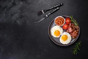 A delicious nutritious healthy breakfast with fried eggs, bacon, beans, a glass of juice, oat cookies, milk and jam photo