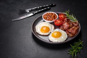 A delicious nutritious healthy breakfast with fried eggs, bacon, beans, a glass of juice, oat cookies, milk and jam photo