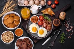 A delicious nutritious healthy breakfast with fried eggs, bacon, beans, a glass of juice, oat cookies, milk and jam photo