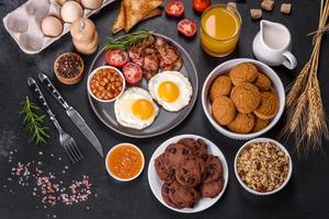 A delicious nutritious healthy breakfast with fried eggs, bacon, beans, a glass of juice, oat cookies, milk and jam photo