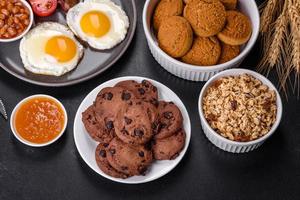 A delicious nutritious healthy breakfast with fried eggs, bacon, beans, a glass of juice, oat cookies, milk and jam photo