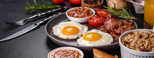 A delicious nutritious healthy breakfast with fried eggs, bacon, beans, a glass of juice, oat cookies, milk and jam photo