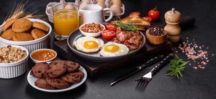 A delicious nutritious healthy breakfast with fried eggs, bacon, beans, a glass of juice, oat cookies, milk and jam photo