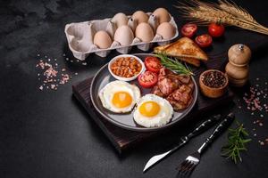 A delicious nutritious healthy breakfast with fried eggs, bacon, beans, a glass of juice, oat cookies, milk and jam photo