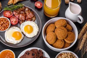 A delicious nutritious healthy breakfast with fried eggs, bacon, beans, a glass of juice, oat cookies, milk and jam photo