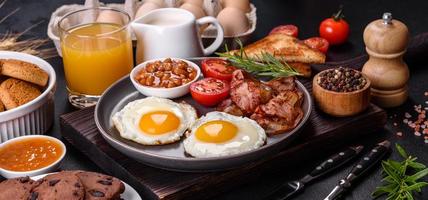 A delicious nutritious healthy breakfast with fried eggs, bacon, beans, a glass of juice, oat cookies, milk and jam photo