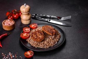 Delicious fresh boiled buckwheat porridge with vegetables and spices on a black plate photo