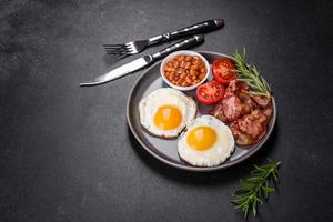 A delicious nutritious healthy breakfast with fried eggs, bacon, beans, a glass of juice, oat cookies, milk and jam photo
