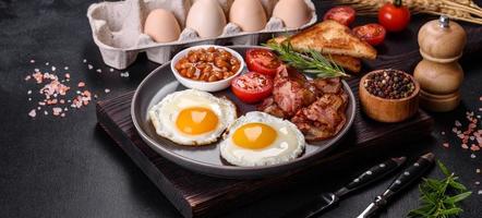 A delicious nutritious healthy breakfast with fried eggs, bacon, beans, a glass of juice, oat cookies, milk and jam photo