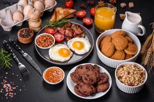 A delicious nutritious healthy breakfast with fried eggs, bacon, beans, a glass of juice, oat cookies, milk and jam photo