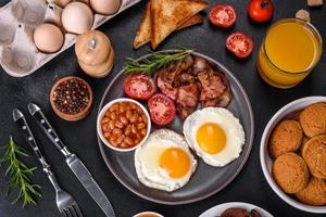 A delicious nutritious healthy breakfast with fried eggs, bacon, beans, a glass of juice, oat cookies, milk and jam photo