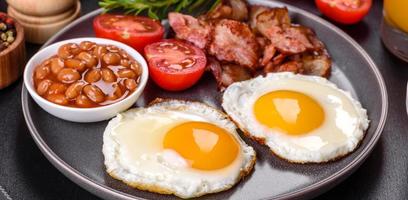 A delicious nutritious healthy breakfast with fried eggs, bacon, beans, a glass of juice, oat cookies, milk and jam photo