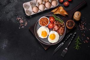 A delicious nutritious healthy breakfast with fried eggs, bacon, beans, a glass of juice, oat cookies, milk and jam photo