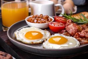 A delicious nutritious healthy breakfast with fried eggs, bacon, beans, a glass of juice, oat cookies, milk and jam photo