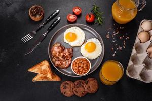 A delicious nutritious healthy breakfast with fried eggs, bacon, beans, a glass of juice, oat cookies, milk and jam photo