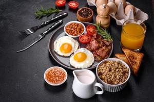 A delicious nutritious healthy breakfast with fried eggs, bacon, beans, a glass of juice, oat cookies, milk and jam photo