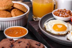 A delicious nutritious healthy breakfast with fried eggs, bacon, beans, a glass of juice, oat cookies, milk and jam photo