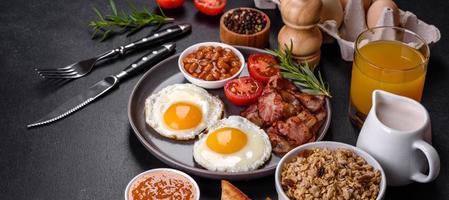 un delicioso desayuno saludable y nutritivo con huevos fritos, tocino, frijoles, un vaso de jugo, galletas de avena, leche y mermelada foto