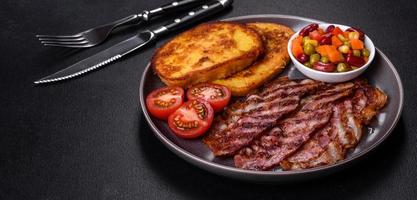 Slices of delicious grilled bacon with croutons fried in egg with spices, salt, vegetables and herbs photo