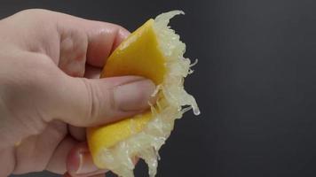 Hand squeezing half of lemon with lime drop on black background. video