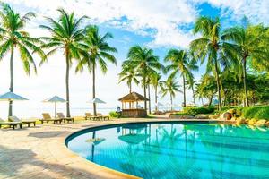Hermosa sombrilla de lujo y una silla alrededor de la piscina al aire libre en el hotel y resort con palmera de coco en el cielo azul foto