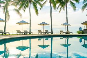 Hermosa sombrilla de lujo y una silla alrededor de la piscina al aire libre en el hotel y resort con palmera de coco en el cielo al atardecer o al amanecer foto
