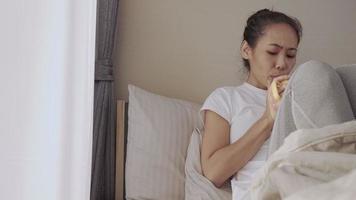 mujer asiática en edad laboral tomando su café mientras se sienta en la cama, antes de salir a trabajar, disfruta de la adicción a la cafeína, estilo de vida cómodo, mujer aislada durante la pandemia de covid, concepto de quedarse en casa video