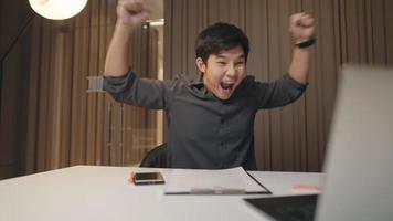 Happy Asian male company worker celebrating at the working desk after done closing business deal with clients online, successful businessman expressing  glad and cheerful emotion, job done complete video