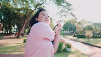 asiatische frau mittleren alters, die morgens im park dehnübungen für arme und schultern macht, ruhestandslebensstil, fitnessgesundheit, training an einem sonnigen tag, vitalitäts-wellness-freizeitaktivitäten video