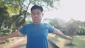 asiatischer mann mittleren alters, der aufwärmübungen im park macht, schwingen und rotierende arme schulter, ruhestandslebensstil, fitnessgesundheitswesen, training an einem sonnigen tag, vitalitätswellness, alterskrankheitsprävention