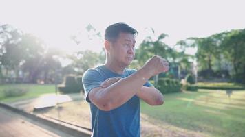 asiatisk medelålders man gör armar axel sträcker uppvärmning träning inne i parken, muskler och leder flexibilitet senior sjukförsäkring, utomhusaktiviteter, vitalitet wellness fitness video