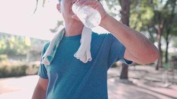 Aziatische man van middelbare leeftijd die vers koud water drinkt uit een plastic fles na het sporten in het park, ouderen trainen, verfrissend drankje, rehydratatie van de levensstijl van de pensionering, water zuiveren mineraalwater, video