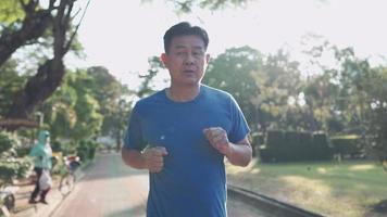 asiatisk senior man springer inne i löparbanan i parken en solig dag i slow motion. pensionslivsstilsaktivitet. hälso-och sjukvård motivation koncept, uthållighet konditionsträning, framifrån video