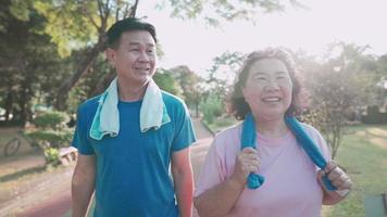 Aziatisch senior paar samen wandelen in zijrecreatie openbaar park, gezonde pensioenlevensstijl, relatiedoel, gelukkig lachend middelbare leeftijd paar oefeningen, familie buitenactiviteiten op zonnige dag video