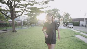 asiatisk kvinna springer stadsdel gatupark på grönt gräs under träd nyanser, i solnedgången, träna motivation, gå ner i vikt kroppskonditionering träning, på diet viktkontroll, slow motion video