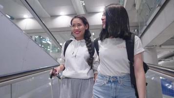 giovani amici felici asiatici attraenti che viaggiano con lo zaino della valigia che camminano parlando sulla passerella della scala mobile, viaggi di vacanza all'estero, migliori amici che si divertono a discutere insieme, concetto di viaggio aereo video