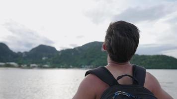 Young asian traveler with backpack showing relief feelings after seeing the beautiful ocean scenic view in front of him,  tropical travel, islands hopping, human and nature environment concept video