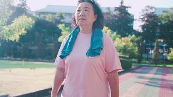 Aziatische oudere vrouw die op een zonnige dag binnen de atletiekbaan in het park loopt, gewichtsverliezende zwaarlijvigheidscontrole, ontspannende oefening, pensioenlevensstijl actieve activiteit, polsbloeddruk volgen