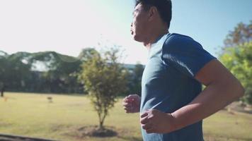 uomo anziano asiatico che corre all'interno del parco in una giornata di sole al rallentatore. attività di stile di vita sano di pensionamento. piano di assicurazione sanitaria per anziani, nella stagione calda estiva, vista laterale video