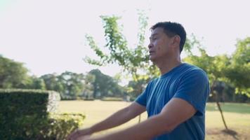 hombre asiático de mediana edad calentando su cuerpo balanceando su brazo antes de correr en el parque al aire libre, en un día soleado, entrenamiento de alto nivel, sintiendo la prevención fresca de enfermedades de ancianos, anciano asiático haciendo ejercicio video