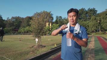 Aziatische senior man drinkwater uit plastic fles rusten na het hardlopen in het buitenpark, pensioen gezonde levensstijl fitness gezondheidszorg, senior buitenactiviteit op zonnige dag, rimpel leeftijden gezicht video