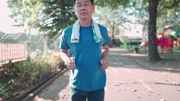 asiatischer mann mittleren alters, der an einem sonnigen tag im park unter bäumen läuft, ruhestandsaktivität für einen gesunden lebensstil. älterer Patient mit ärztlicher Empfehlung, heißes Sommerwetter, Fitnessmotivation trainieren video