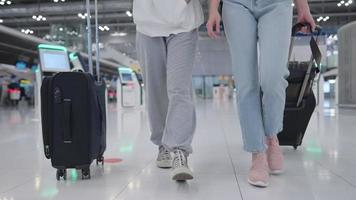 Low angle shot of two female passengers dragging their suitcase baggage trolley walking along the airport aisles, two passengers arrive at departure terminal travel booking reservation, slow motion video