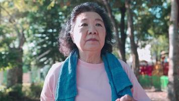 asiatische Seniorin, die an einem sonnigen Tag in Zeitlupe im Übungspark im Schatten der Bäume läuft. Ruhestands-Lifestyle-Aktivität. Gesundheitsmotivation, Puls-Blutdruck-Verfolgung, Handaufnahme